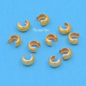 May include: Ten gold-colored crimp beads, used for jewelry making, are scattered on a blue background. The crimp beads are small, round, and have a hole in the center.