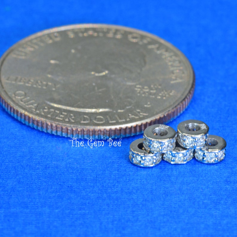 May include: Five silver-toned rings with clear sparkling stones set in a row. The rings are small and are shown next to a US quarter for size comparison.
