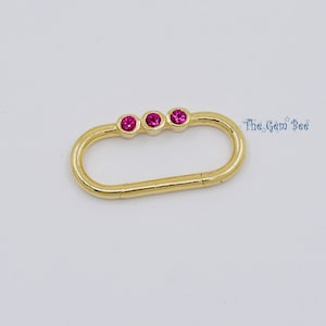 May include: Gold-toned oval-shaped charm with three pink gemstones. The charm has a clasp on one side.
