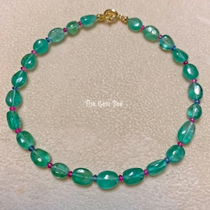 Op de afbeelding: Een ketting met gladde, ovaalvormige groene kralen afgewisseld met kleine, felroze en blauwe accentkralen. Het snoer is bevestigd met een goudkleurige metalen sluiting. De tekst The Gem Bee staat in het midden van de cirkelvormige opstelling.