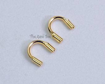 May include: Two gold-colored U-shaped metal crimp ends with a smooth, polished finish. Each piece features a curved bridge connecting two parallel cylindrical tubes. The text The Gem Bee is printed in a dark font between the two metal components.