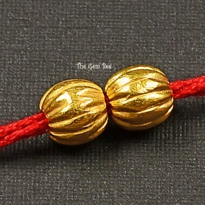 Peut inclure: Deux perles dorées texturées enfilées sur un cordon rouge. Les perles sont rondes et légèrement ovales.