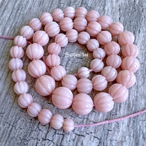 Könnte beinhalten: Eine Strähne aus rosa geschnitzten Edelsteinperlen. Die Perlen sind rund und haben ein geschnitztes Design, das einer Blume ähnelt. Die Perlen sind auf einem rosa Faden aufgereiht.
