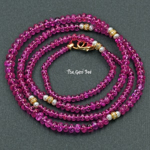 May include: A multi-strand necklace made of pink gemstones and small white pearls with gold accents. The necklace has a clasp closure.