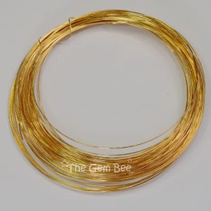 May include: A continuous coil of thin, flexible gold-colored craft wire arranged in a circular loop. The wire has a smooth, metallic finish and a reflective surface. The text "The Gem Bee" is printed in white at the bottom of the wire coil.