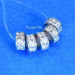 May include: Six silver-toned spacer beads with clear rhinestones. The beads are arranged in a circle on a blue background.