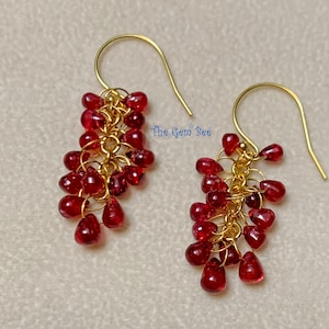 May include: Gold earrings with a cascade of red gemstone beads. The earrings are made with a delicate chain design and feature a teardrop shape.