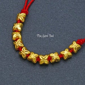 May include: A gold bracelet with a red string and gold flower-shaped beads. The bracelet is tied with a knot at the end.