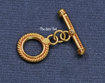 May include: A gold-toned toggle clasp for jewelry featuring a circular ring with a twisted rope texture and a matching T-bar component. The two pieces are connected by two small jump rings. The text The Gem Bee is visible in the center.