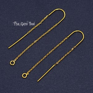 May include: A pair of gold-colored threader earrings. Each earring features a long, straight post that curves into a U-shape, connected to a delicate chain. The chain ends with a small, round loop. The Gem Bee logo is in the upper left corner.