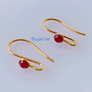 May include: A pair of gold earrings with red gemstone accents. The earrings are simple and elegant, perfect for everyday wear.
