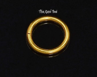 May include: A circular gold-colored metal ring with a smooth, polished finish and a visible seam. The text The Gem Bee is printed in white above the ring. The object is presented against a solid black background, highlighting its metallic luster.