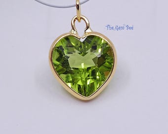 May include: A heart-shaped pendant featuring a faceted lime green gemstone set in a polished gold-tone metal bezel. The pendant includes a small gold-tone bail at the top for attachment. The text The Gem Bee is printed in blue near the top right.