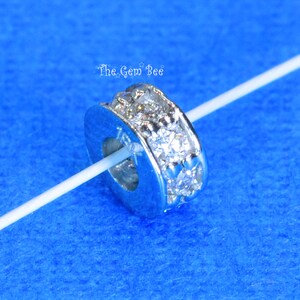 May include: Silver charm bead featuring a row of clear cubic zirconia stones. The bead has a round hole in the centre for threading onto a bracelet or necklace.