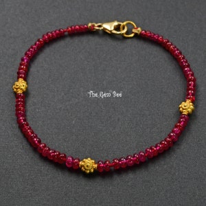 Op de afbeelding: Een rode edelsteen armband met gouden accenten. De armband is gemaakt van kleine, ronde rode edelstenen en heeft drie gouden bloemvormige bedels.