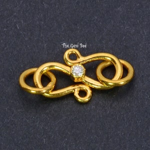 May include: Gold-toned clasp with a clear rhinestone in the center. The clasp is designed in a figure eight shape with a decorative twist.