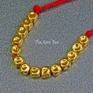 May include: A gold bracelet with a red string and gold beads. The beads are square shaped and have a textured surface.