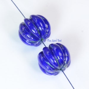 May include: Two blue lapis lazuli beads with a ribbed texture. The beads are strung on a wire.