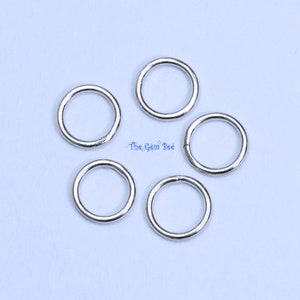 May include: Five silver jump rings, each with a circular shape, are arranged on a white surface. The rings are approximately 1/2 inch in diameter.