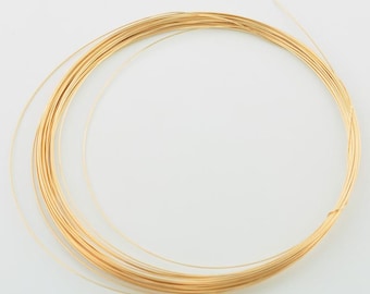 May include: A continuous coil of thin, flexible gold-colored metal wire arranged in a circular pattern. The wire has a smooth, reflective surface and a consistent gauge throughout the entire length of the spool, forming multiple overlapping loops.