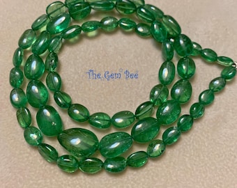 Puede incluir: Un collar de cuentas ovaladas verdes, pulidas y translúcidas, dispuestas en un patrón circular. Las cuentas varían en tamaño y presentan un tono esmeralda vibrante con inclusiones naturales. El texto The Gem Bee está impreso en azul en el centro.