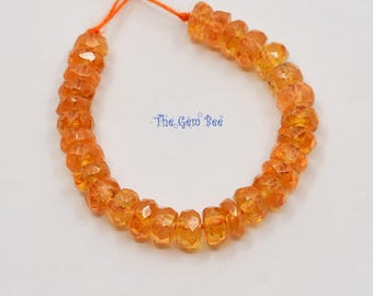 May include: A strand of faceted, translucent orange gemstone beads arranged in a circular shape on a string. The beads have a uniform, round, flat-edged design. The text The Gem Bee is printed in blue in the center of the bead arrangement.