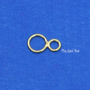 May include: Gold-toned metal connector with two circles, one larger than the other, connected by a small bar. The connector is on a blue background.