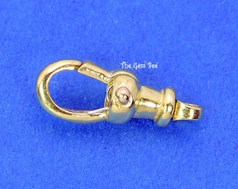 May include: A gold-toned metal lobster claw clasp featuring a spring-loaded mechanism and a swivel base. The surface is polished and reflective. The text The Gem Bee is printed in white near the center of the clasp, which is oriented horizontally.