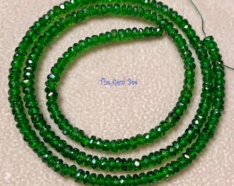 Puede incluir: Una hebra de pequeñas cuentas de piedras preciosas facetadas de color verde vibrante dispuestas en un patrón circular. Las cuentas son uniformes en tamaño y forma, con una superficie reflectante. El texto "The Gem Bee" aparece en azul en el centro.