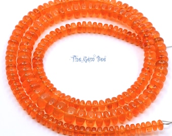 May include: A long strand of translucent orange rondelle-shaped beads arranged in a circular pattern. The beads have a smooth, polished finish and a consistent vibrant color. The text The Gem Bee is printed in blue in the center of the circle.