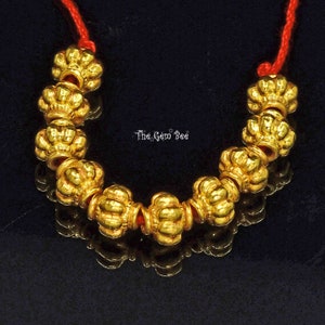 May include: A gold necklace with a red string and ornate gold beads. The beads are shaped like a flower with a crown on top.
