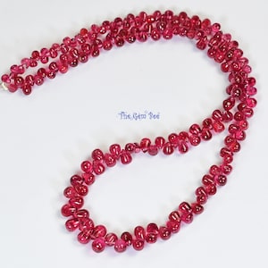 May include: A strand of pink ruby beads in a teardrop shape. The beads are strung on a silver chain.