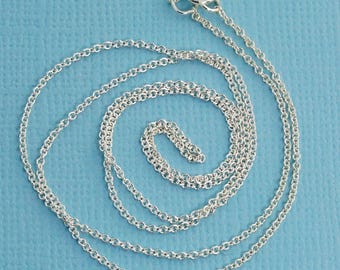 Puede incluir: Un collar de cadena plateada que presenta pequeños eslabones circulares uniformes conectados en un patrón continuo. El collar incluye un cierre de resorte circular en la parte superior, diseñado para asegurar los extremos de la cadena con sencillez.