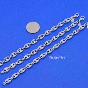 May include: Three silver-colored chain bracelets with a coffee bean link design are displayed on a blue surface. Each bracelet has a lobster clasp closure. A coin is placed near the bracelets.