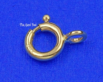 May include: A gold spring ring clasp featuring a circular design with a small protruding lever and a fixed jump ring attachment. The metal surface is polished and includes the stamped text 750, with the watermark The Gem Bee visible.