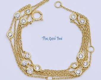 May include: A multi-strand gold chain bracelet featuring several bezel-set round clear stones distributed along the delicate links. The bracelet includes a circular spring ring clasp and displays the text The Gem Bee in blue lettering.
