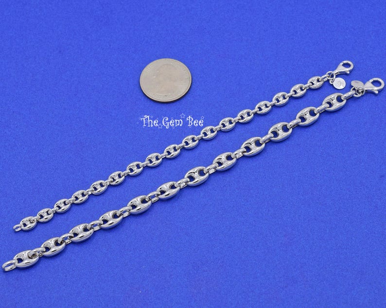 May include: Two silver-toned chain bracelets with a polished finish, featuring a distinctive oval link design. The bracelets are displayed on a blue background, with a coin for size comparison. The Gem Bee is printed on the background.