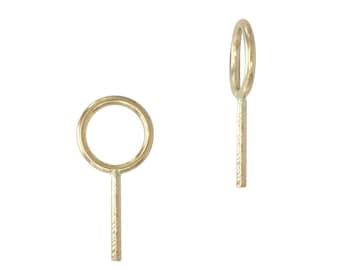 May include: A pair of gold-toned earrings, each featuring a circular hoop attached to a straight, textured vertical bar. The design is simple and geometric, with one earring shown from the front and the other angled to show the side profile.