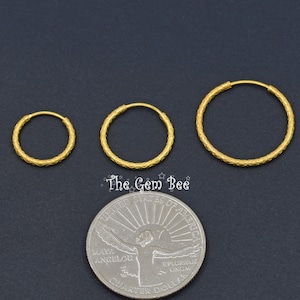 Puede incluir: Tres aros dorados de diferentes tama&ntilde;os dispuestos en fila sobre una moneda de veinticinco centavos de d&oacute;lar estadounidense. Cada aro presenta una superficie texturizada con patr&oacute;n entrecruzado. El texto The Gem Bee aparece en blanco sobre la moneda.