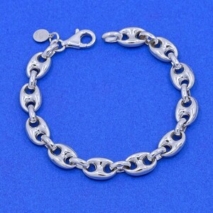 May include: A silver-colored bracelet with a series of oval-shaped links, connected to each other. The bracelet has a lobster clasp closure and a small circular charm. The jewelry is displayed against a blue background.