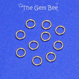 May include: Ten gold jump rings on a blue background. The jump rings are small and circular.