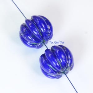May include: Two deep blue, pumpkin-shaped beads with vertical ridges and subtle gold-colored flecks, strung on a thin dark thread. The beads feature a glossy finish and are marked with the text The Gem Bee in small blue lettering between them.