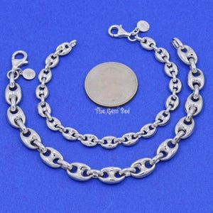 May include: Two silver-toned chain bracelets with a polished finish, featuring a unique oval link design. The bracelets are displayed on a blue surface next to a US quarter coin. The Gem Bee is printed on the coin.