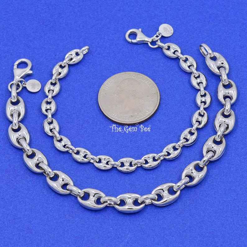 May include: Two silver-toned chain bracelets with a polished finish, featuring a unique oval link design. The bracelets are displayed on a blue surface next to a US quarter coin. The Gem Bee is printed on the coin.