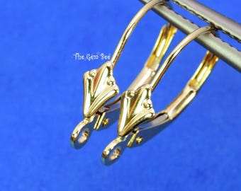 May include: A pair of gold-toned leverback earring findings with a decorative leaf-shaped front element and a small circular loop at the base for attaching charms. The text The Gem Bee is visible in the upper left area of the image.