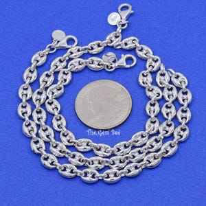 May include: A close-up shot of a silver-colored chain necklace with a unique puffed mariner link design. The necklace is displayed on a blue surface next to a quarter coin for size reference. The Gem Bee logo is visible.