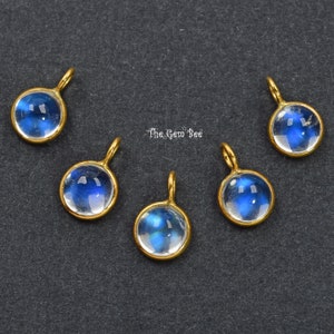 Puede incluir: Seis colgantes de tono dorado con cabujones redondos de piedra lunar transparente. Cada colgante tiene un pequeño bucle para sujetarlo a una cadena o cordón.