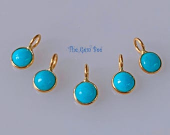 May include: Five small circular charms featuring smooth, bright turquoise cabochons set in polished gold-toned metal frames. Each charm includes a small gold-toned jump ring at the top for attachment. The text The Gem Bee is visible in blue.