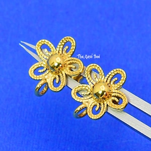May include: A pair of gold-tone flower-shaped earrings with a textured design. The earrings are held together by a pair of tweezers.