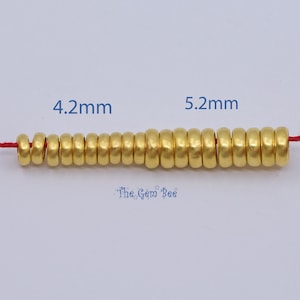 May include: A strand of gold-colored beads, ranging from 4.2mm to 5.2mm in diameter, strung on a red cord. The beads have a cylindrical shape and a matte finish. The text "The Gem Bee" is visible at the bottom.
